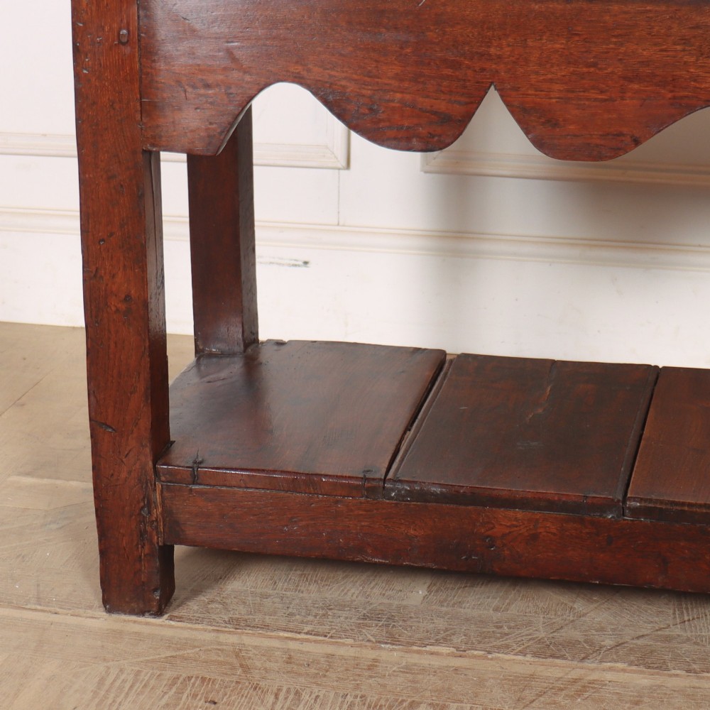 An antique dark oak Welsh dresser base featuring two drawers with brass swan-neck handles, a scalloped apron, and a lower potboard shelf. View III