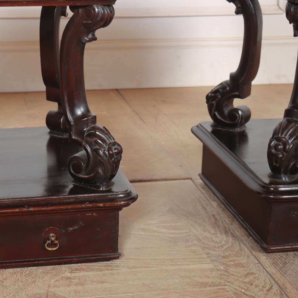 A pair of dark mahogany bedside tables featuring carved scroll supports, upper and lower drawers with brass drop-ring handles, resting on solid plinth bases. View IV