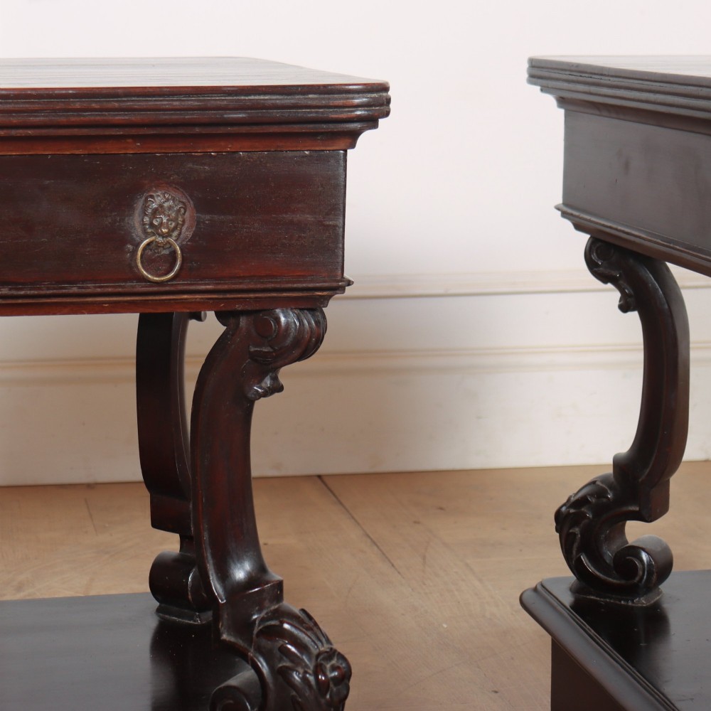 A pair of dark mahogany bedside tables featuring carved scroll supports, upper and lower drawers with brass drop-ring handles, resting on solid plinth bases. View V