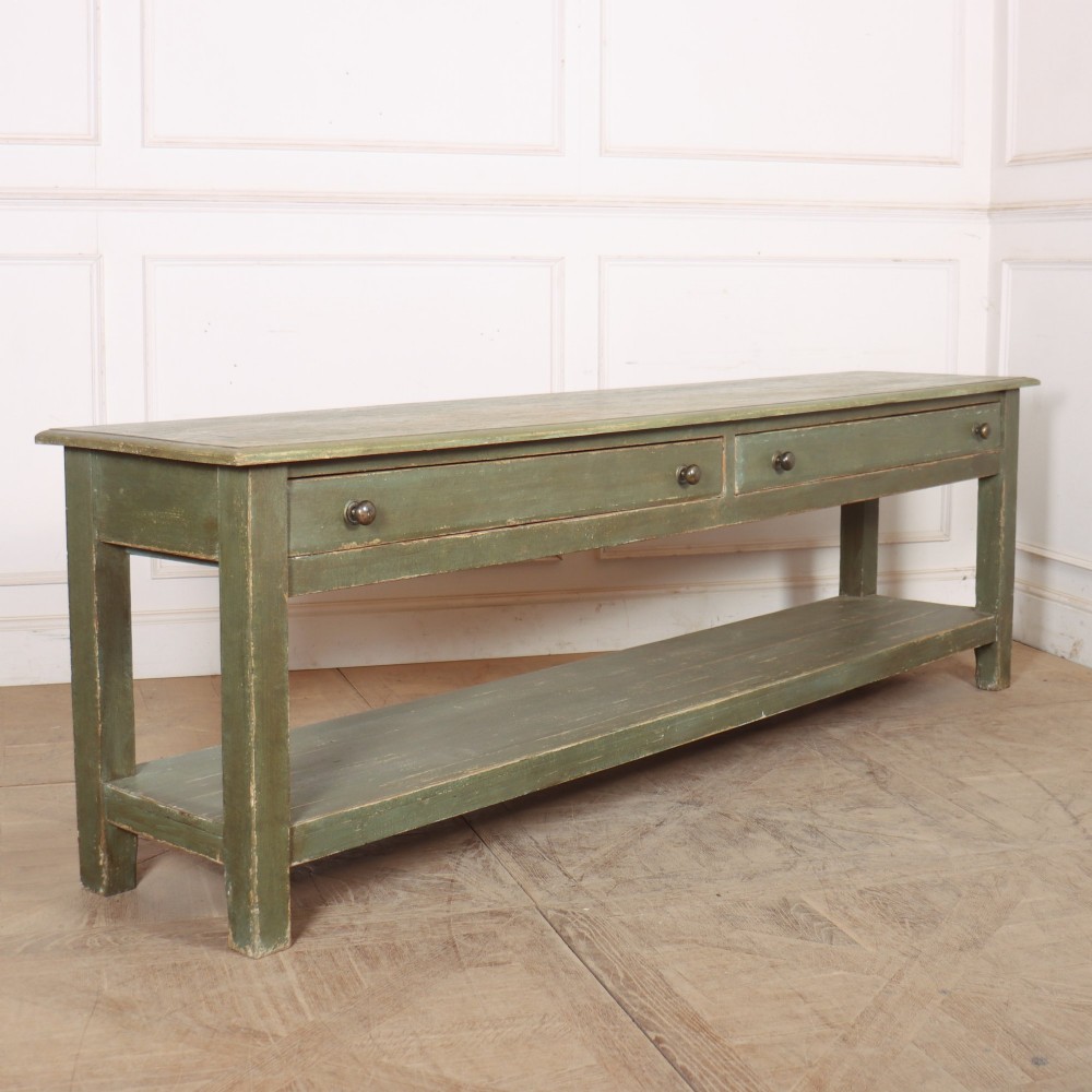 A long muted green painted wooden potboard serving table featuring two drawers with small brass handles and an open lower shelf.