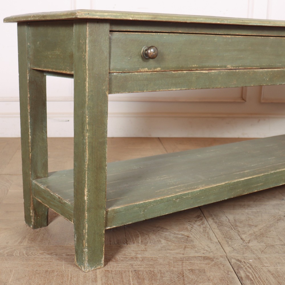 A long muted green painted wooden potboard serving table featuring two drawers with small brass handles and an open lower shelf. View III