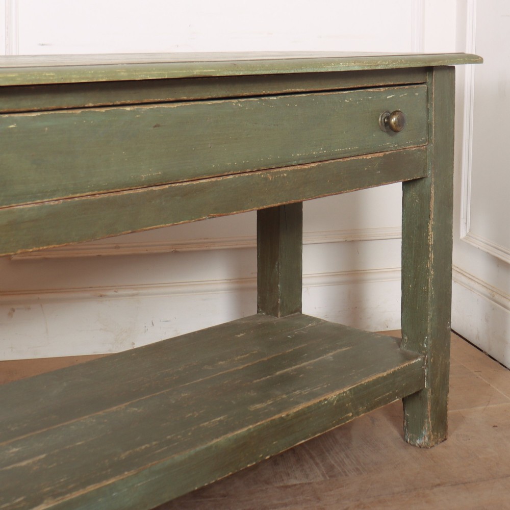 A long muted green painted wooden potboard serving table featuring two drawers with small brass handles and an open lower shelf. View VI
