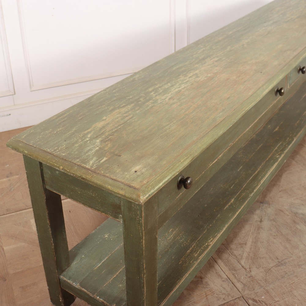 A long muted green painted wooden potboard serving table featuring two drawers with small brass handles and an open lower shelf. View VIII