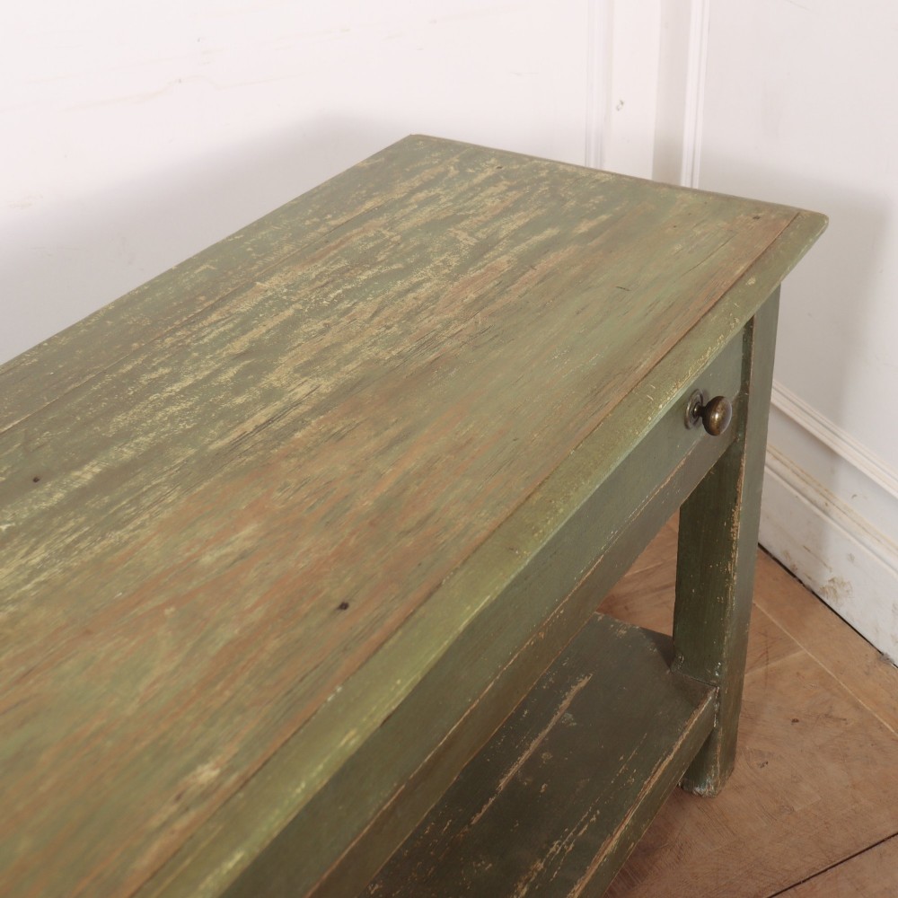 A long muted green painted wooden potboard serving table featuring two drawers with small brass handles and an open lower shelf. View IX