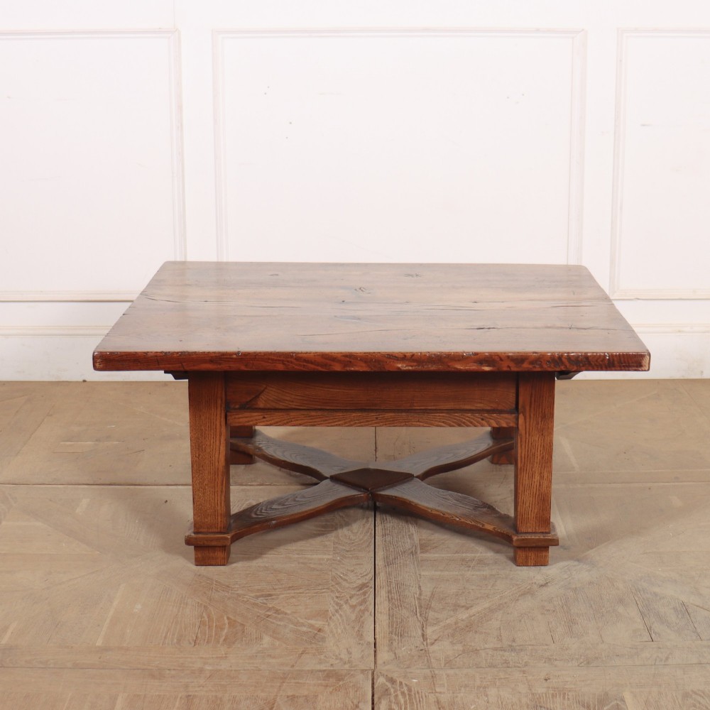A rectangular warm brown solid elm coffee table with a thick plank top and a distinctive X-shaped lower stretcher base.