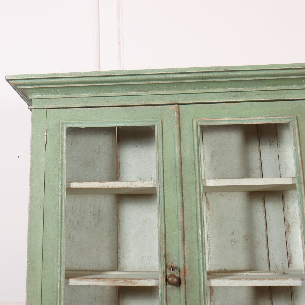 A large sage green painted wooden kitchen dresser with three upper glazed cabinet doors and three lower solid panelled doors. View II