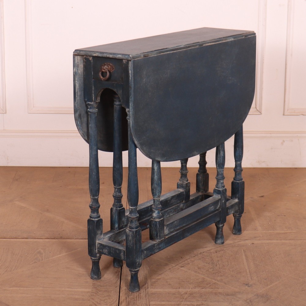 A blue painted antique spider leg drop-leaf table shown with its hinged side leaves folded down, revealing slender turned legs and stretchers.