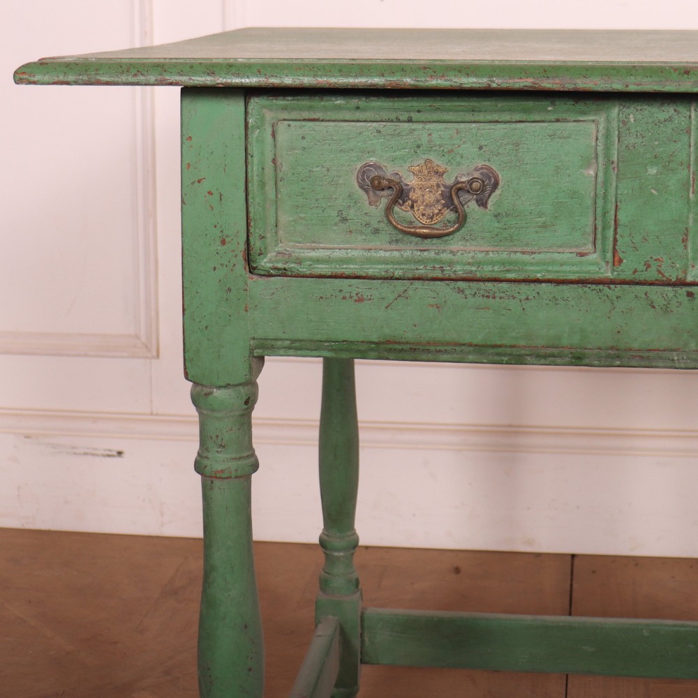 An antique English oak lamp table featuring a distressed green painted finish, two drawers with brass handles, turned legs, and a lower stretcher base. View II