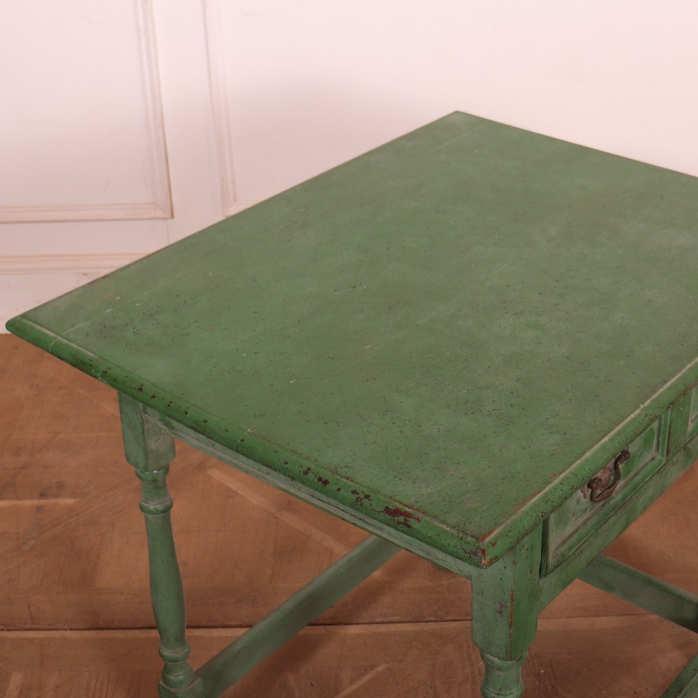 An antique English oak lamp table featuring a distressed green painted finish, two drawers with brass handles, turned legs, and a lower stretcher base. View VII
