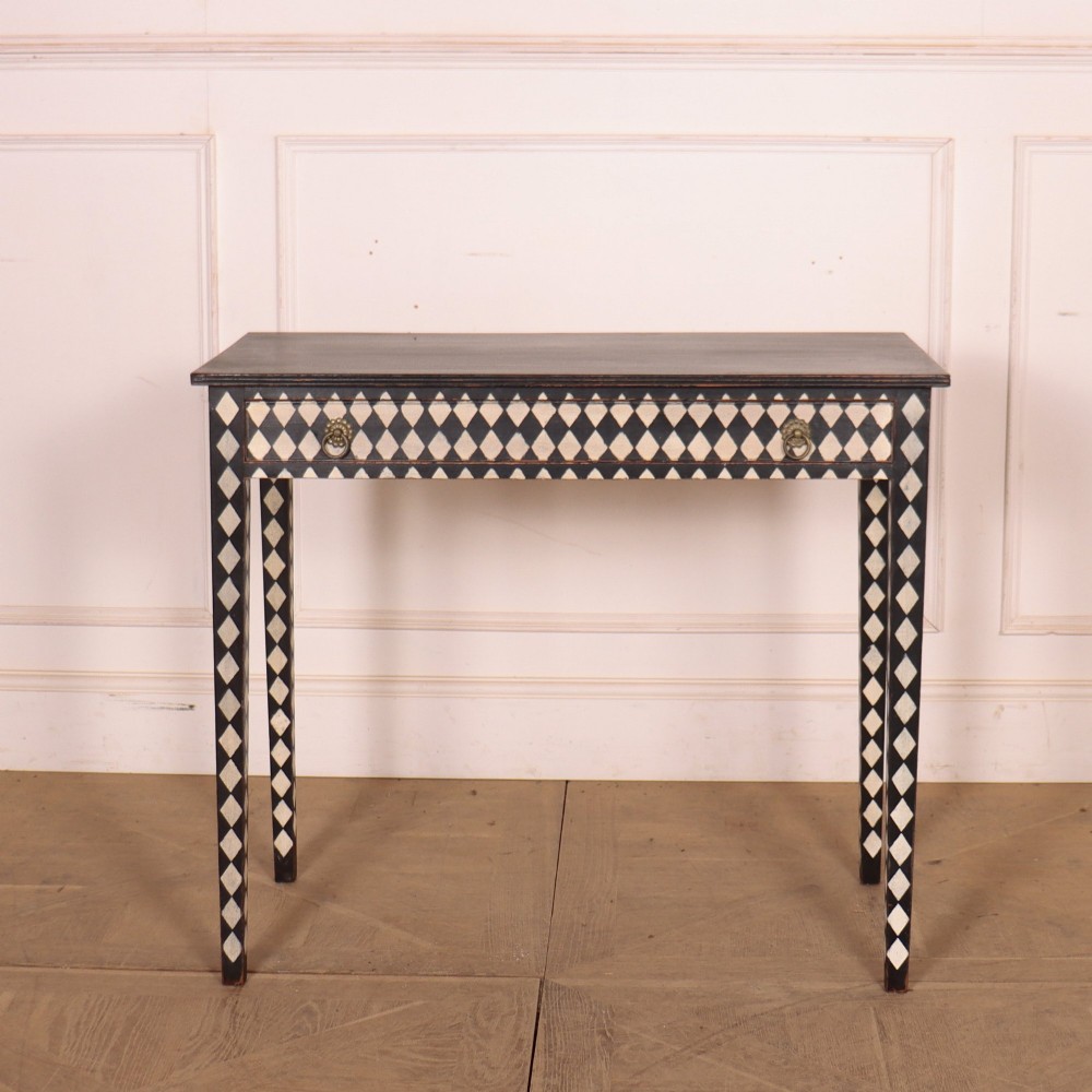 A rectangular black painted lamp table featuring a hand-painted cream and black harlequin diamond pattern on the front drawer and square legs, finished with two brass ring pull handles.