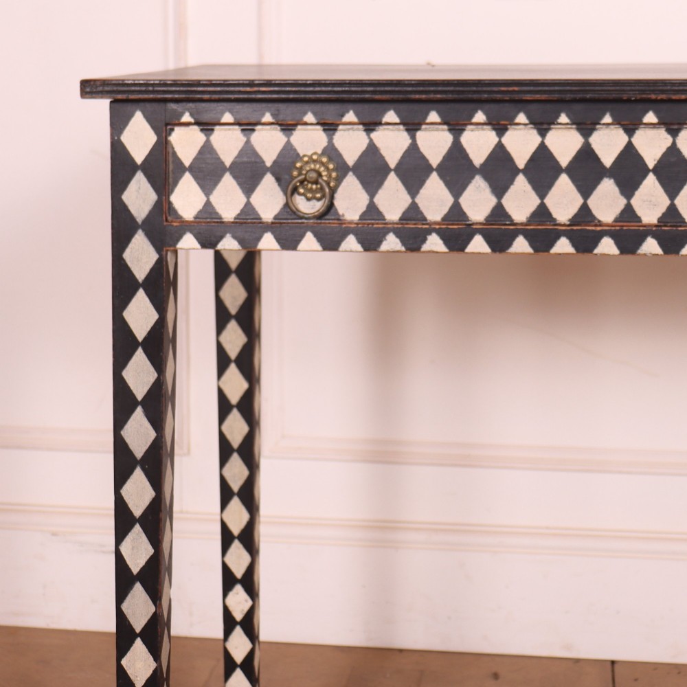 A rectangular black painted lamp table featuring a hand-painted cream and black harlequin diamond pattern on the front drawer and square legs, finished with two brass ring pull handles. View II