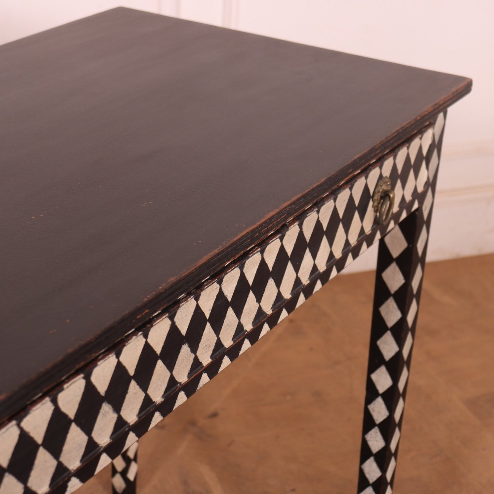A rectangular black painted lamp table featuring a hand-painted cream and black harlequin diamond pattern on the front drawer and square legs, finished with two brass ring pull handles. View VIII