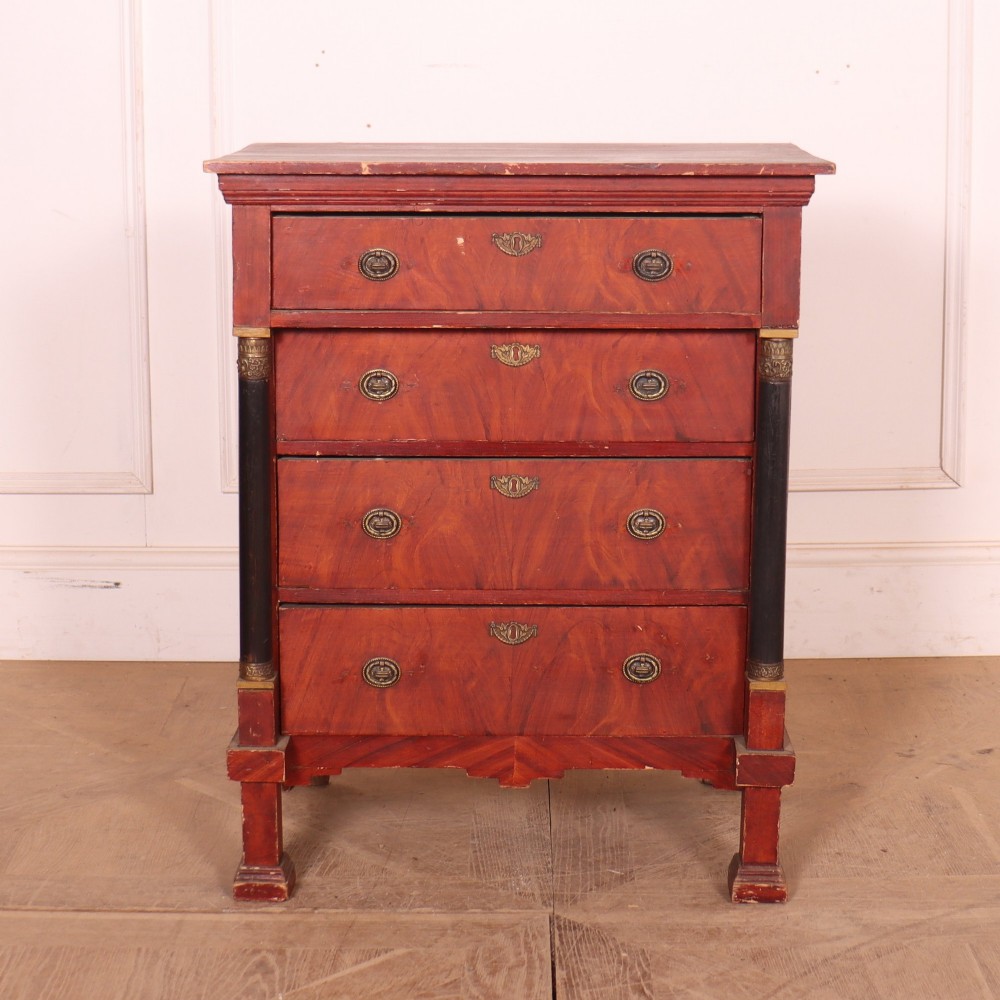 A Dutch Empire style red mahogany commode with four drawers, ebonised side columns, and round brass handles.