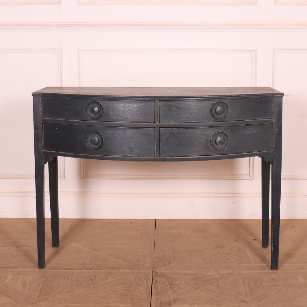 A dark painted antique bowfront console table featuring four drawers with circular wooden knob handles and slender square tapered legs.