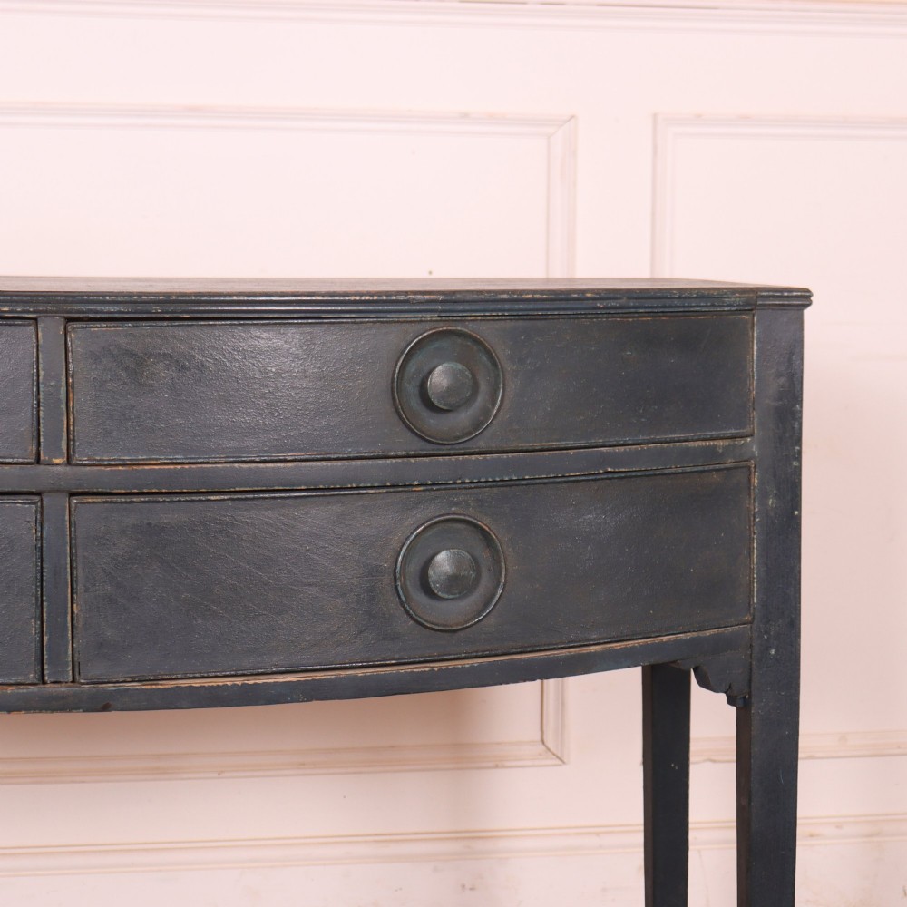 A dark painted antique bowfront console table featuring four drawers with circular wooden knob handles and slender square tapered legs. View III