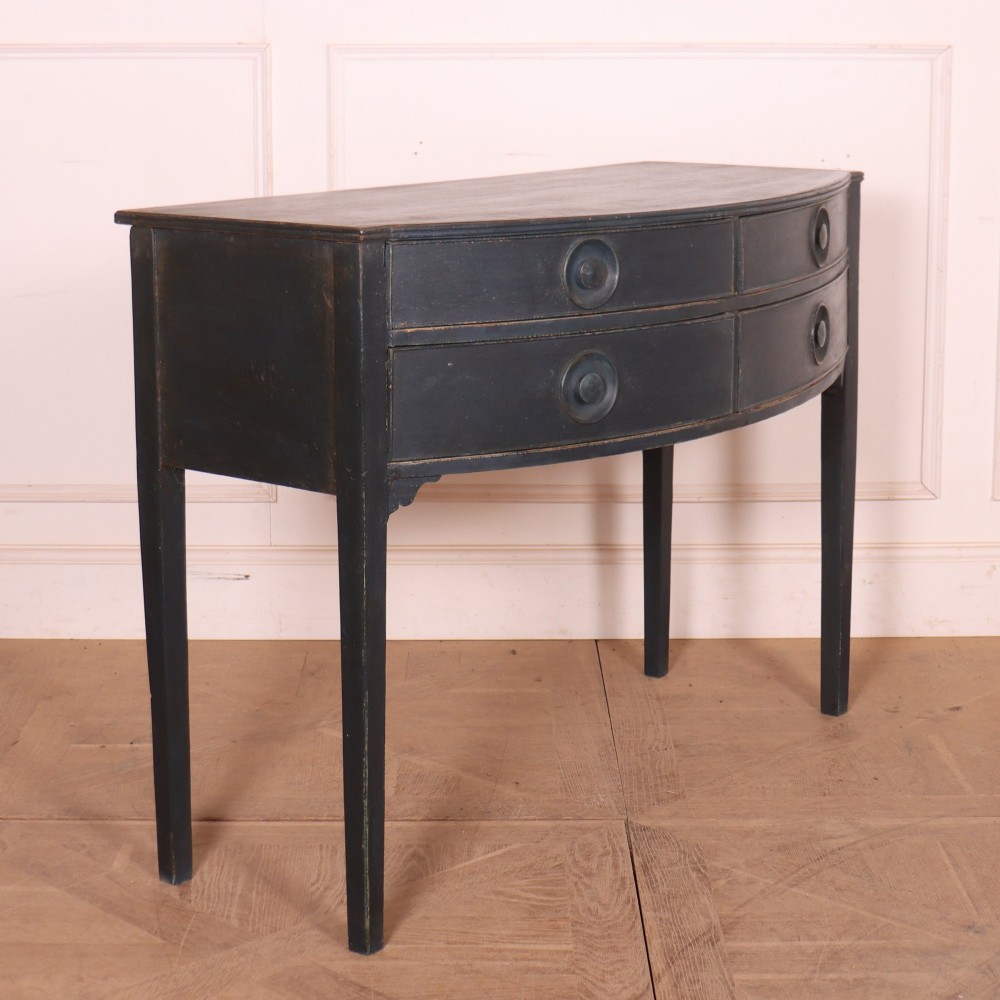 A dark painted antique bowfront console table featuring four drawers with circular wooden knob handles and slender square tapered legs. View VI