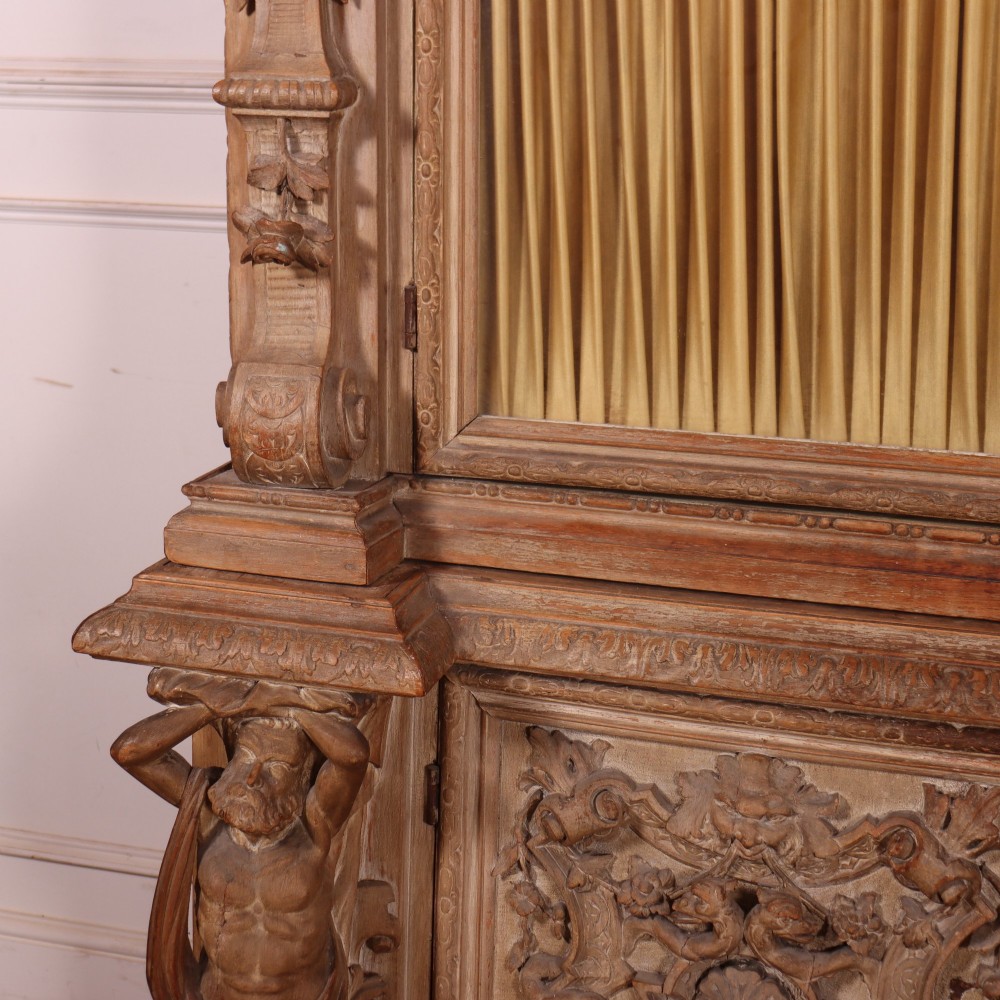 A large Italian carved wood vitrine featuring arched upper glazed doors lined with fabric, flanked by caryatid figures and intricate relief panels. View V