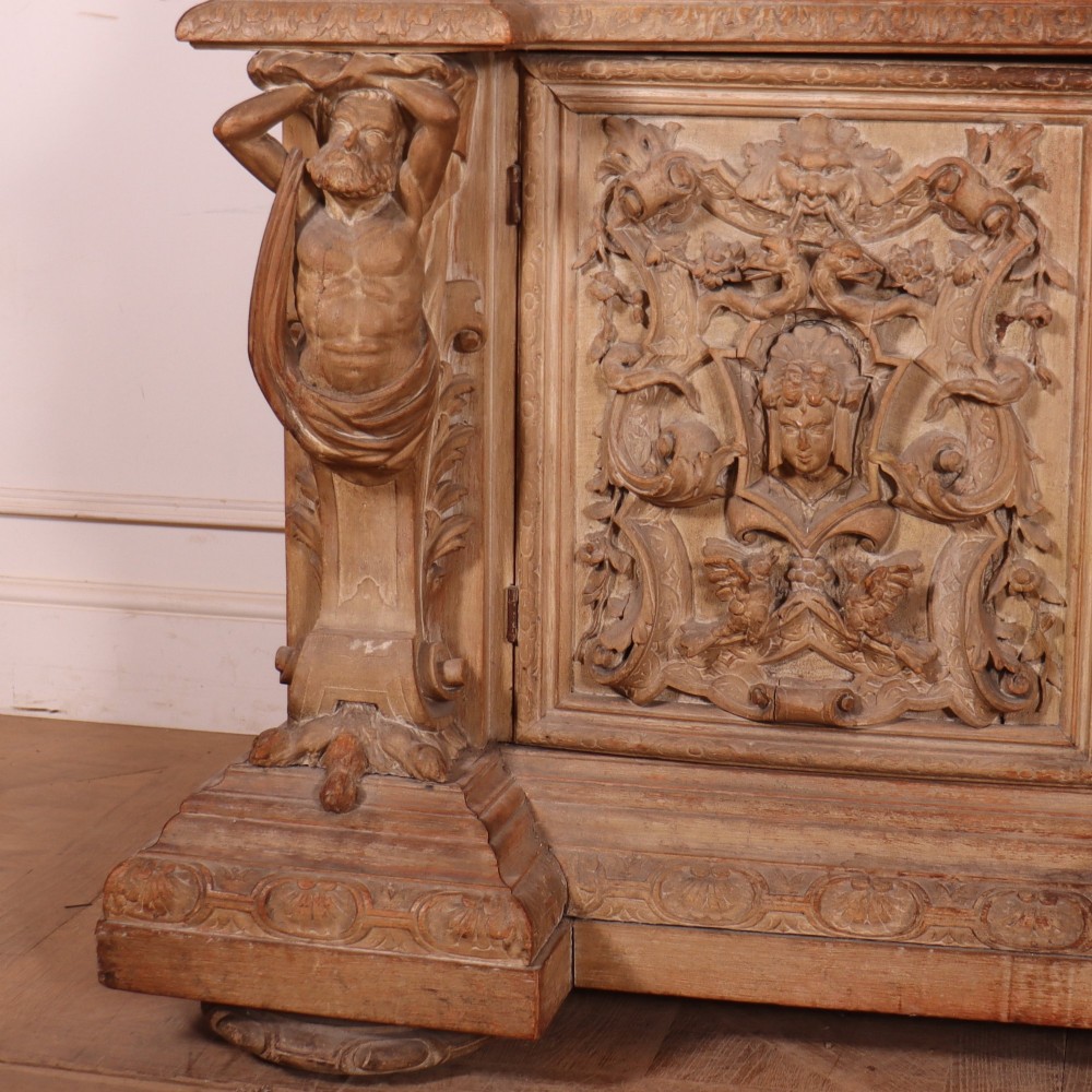 A large Italian carved wood vitrine featuring arched upper glazed doors lined with fabric, flanked by caryatid figures and intricate relief panels. View VII