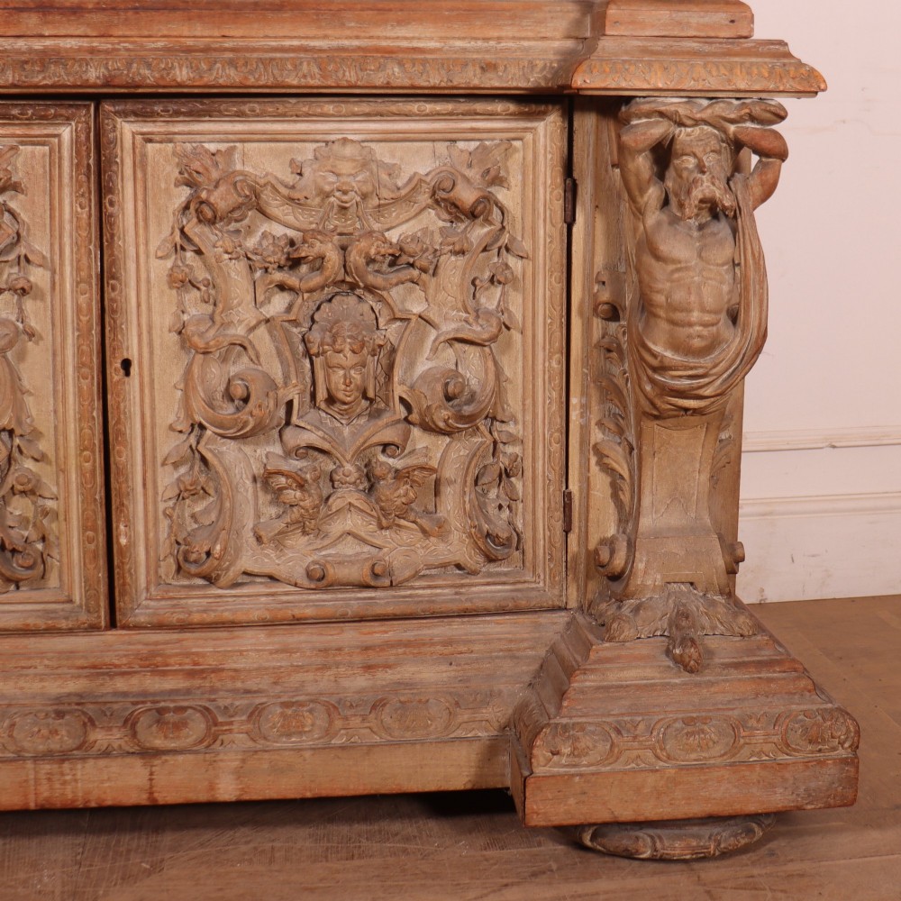 A large Italian carved wood vitrine featuring arched upper glazed doors lined with fabric, flanked by caryatid figures and intricate relief panels. View VIII