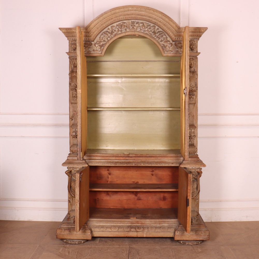 A large Italian carved wood vitrine featuring arched upper glazed doors lined with fabric, flanked by caryatid figures and intricate relief panels. View XI