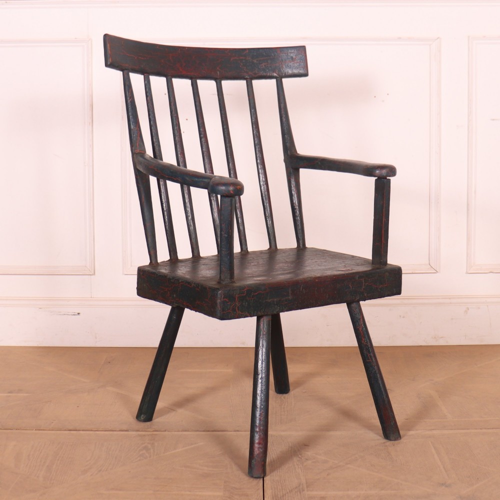 An antique dark green painted Irish primitive armchair featuring a thick wooden slab seat, spindle backrest, flat armrests, and splayed legs.