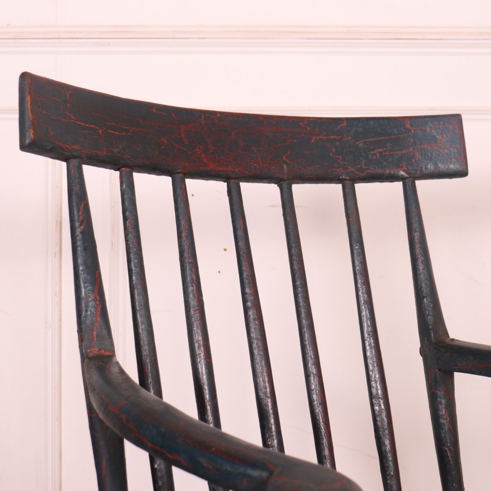 An antique dark green painted Irish primitive armchair featuring a thick wooden slab seat, spindle backrest, flat armrests, and splayed legs. View IV