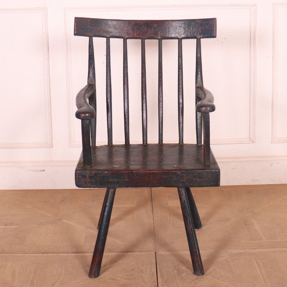 An antique dark green painted Irish primitive armchair featuring a thick wooden slab seat, spindle backrest, flat armrests, and splayed legs. View V