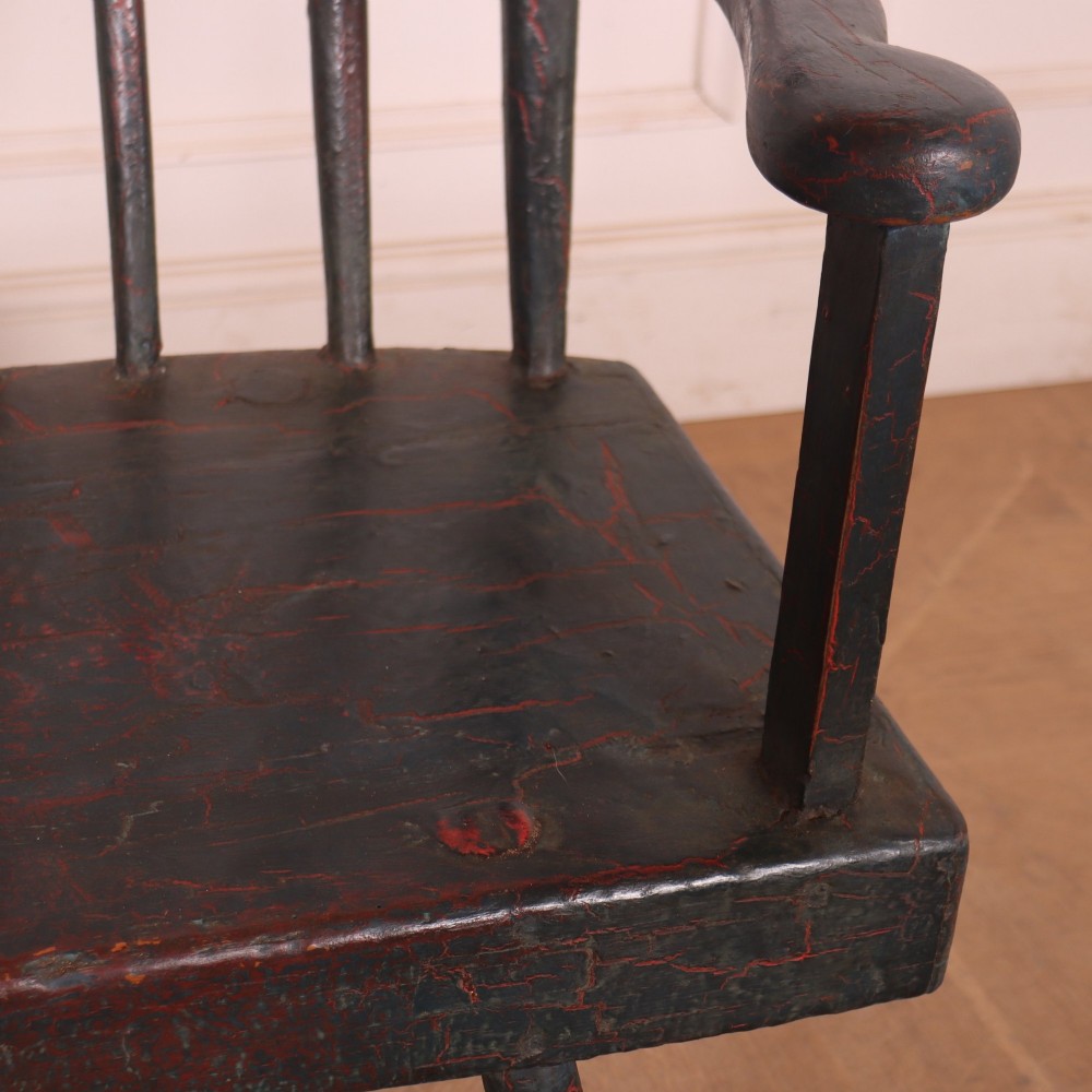 An antique dark green painted Irish primitive armchair featuring a thick wooden slab seat, spindle backrest, flat armrests, and splayed legs. View VI