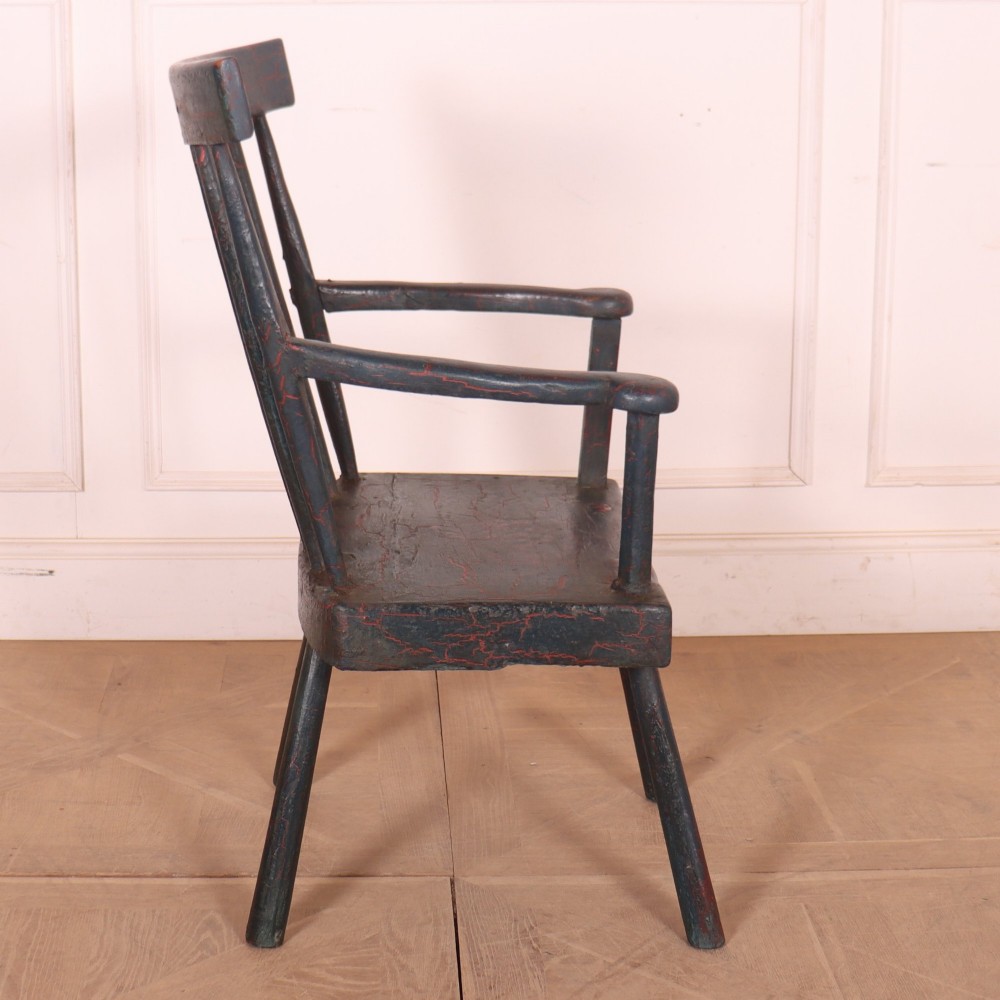 An antique dark green painted Irish primitive armchair featuring a thick wooden slab seat, spindle backrest, flat armrests, and splayed legs. View VIII
