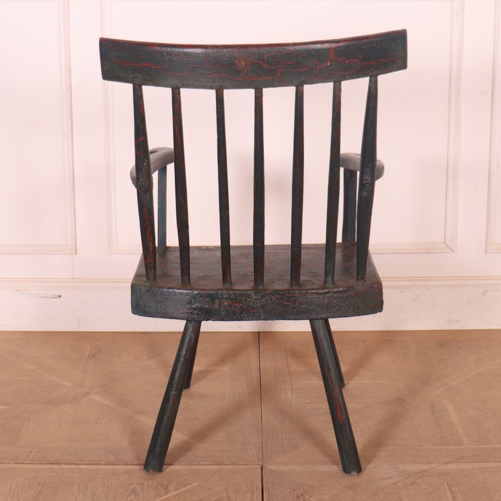 An antique dark green painted Irish primitive armchair featuring a thick wooden slab seat, spindle backrest, flat armrests, and splayed legs. View IX