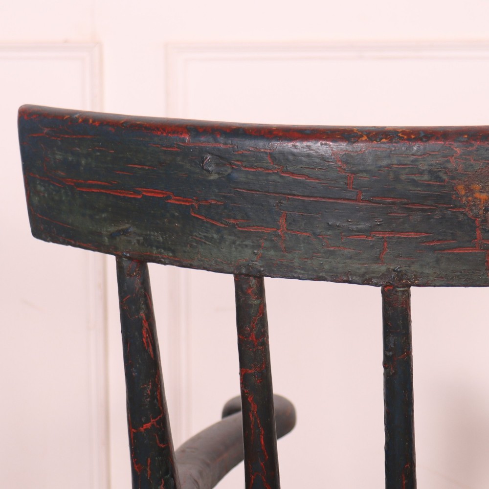 An antique dark green painted Irish primitive armchair featuring a thick wooden slab seat, spindle backrest, flat armrests, and splayed legs. View X