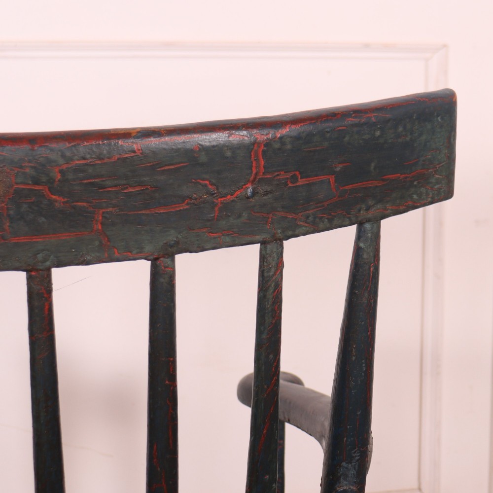 An antique dark green painted Irish primitive armchair featuring a thick wooden slab seat, spindle backrest, flat armrests, and splayed legs. View XI