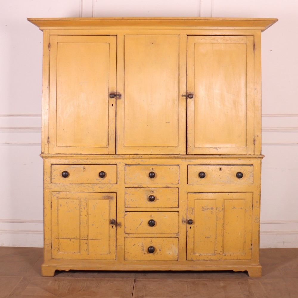 A large antique yellow-painted housekeeper cupboard featuring three upper cupboard doors above an arrangement of drawers and lower cupboards. View II
