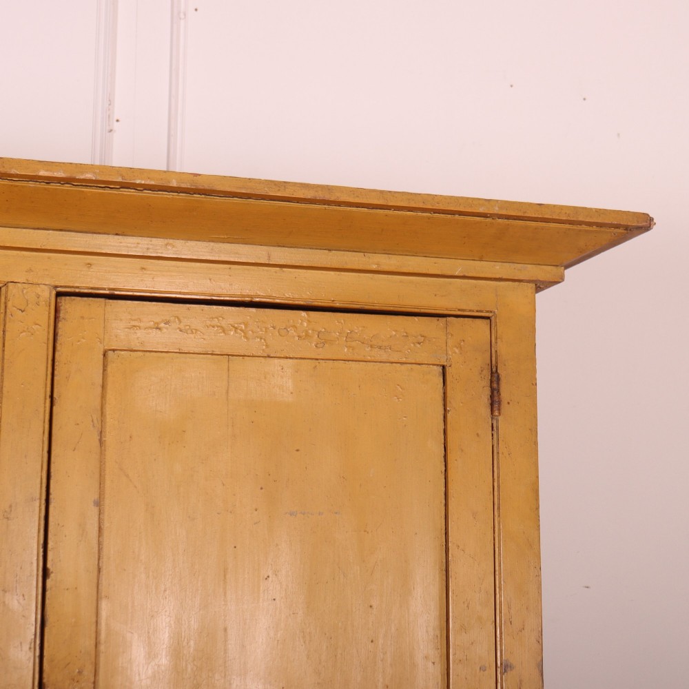 A large antique yellow-painted housekeeper cupboard featuring three upper cupboard doors above an arrangement of drawers and lower cupboards. View IV