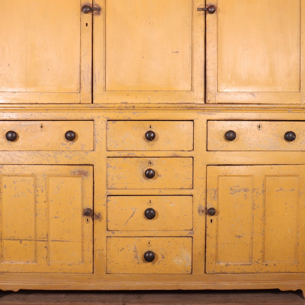 A large antique yellow-painted housekeeper cupboard featuring three upper cupboard doors above an arrangement of drawers and lower cupboards. View VI