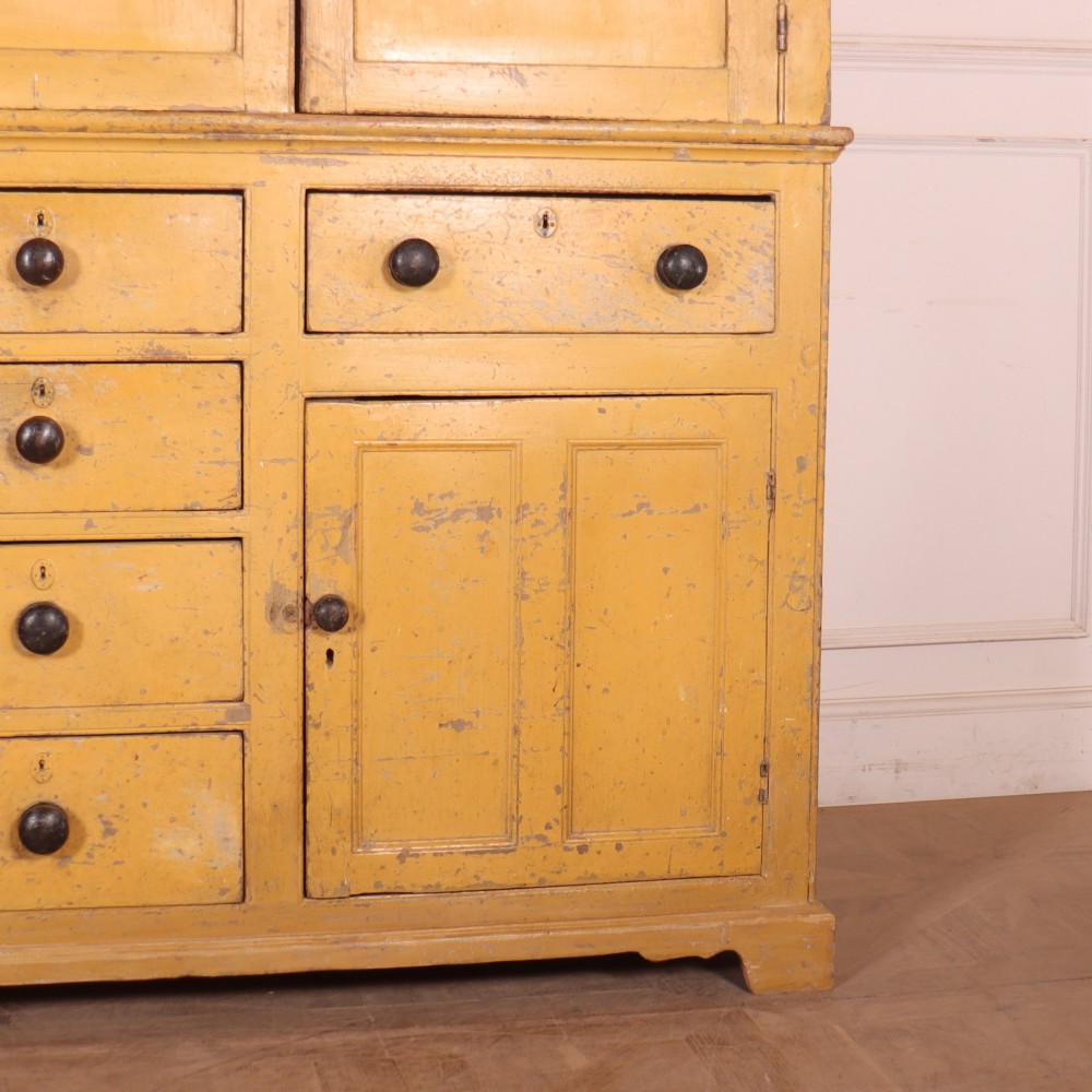 A large antique yellow-painted housekeeper cupboard featuring three upper cupboard doors above an arrangement of drawers and lower cupboards. View VII