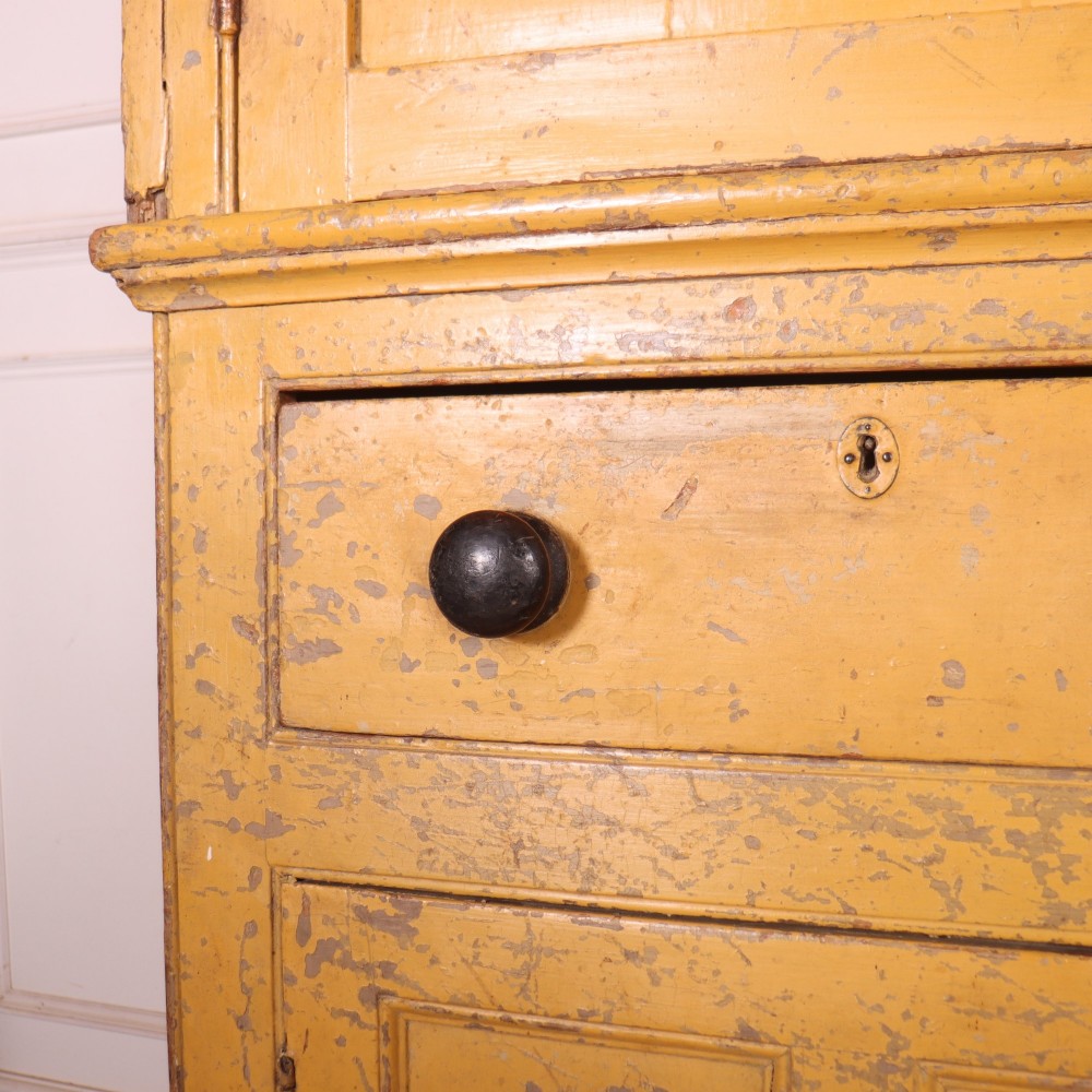 A large antique yellow-painted housekeeper cupboard featuring three upper cupboard doors above an arrangement of drawers and lower cupboards. View X
