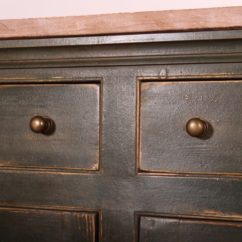 A long dark green painted wooden dresser base featuring four upper drawers over four panelled cupboard doors with a natural timber top. View V