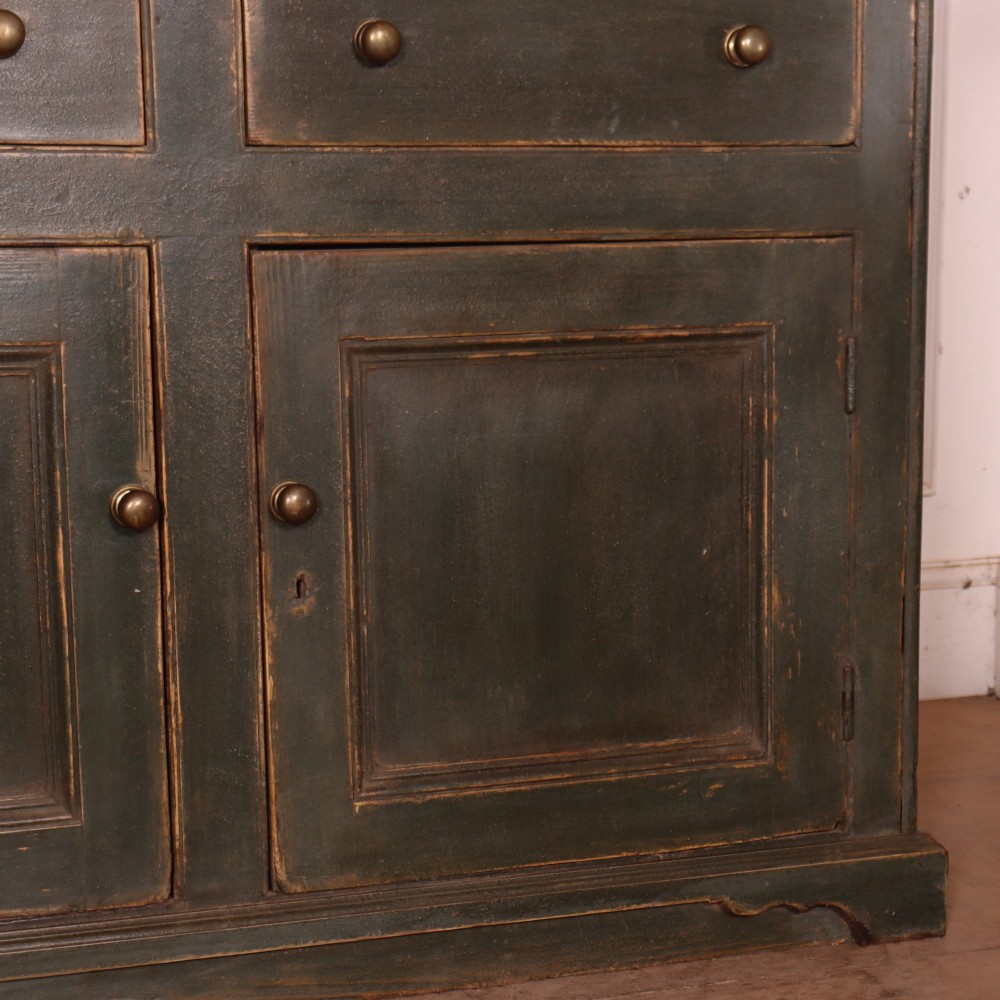 A long dark green painted wooden dresser base featuring four upper drawers over four panelled cupboard doors with a natural timber top. View IX