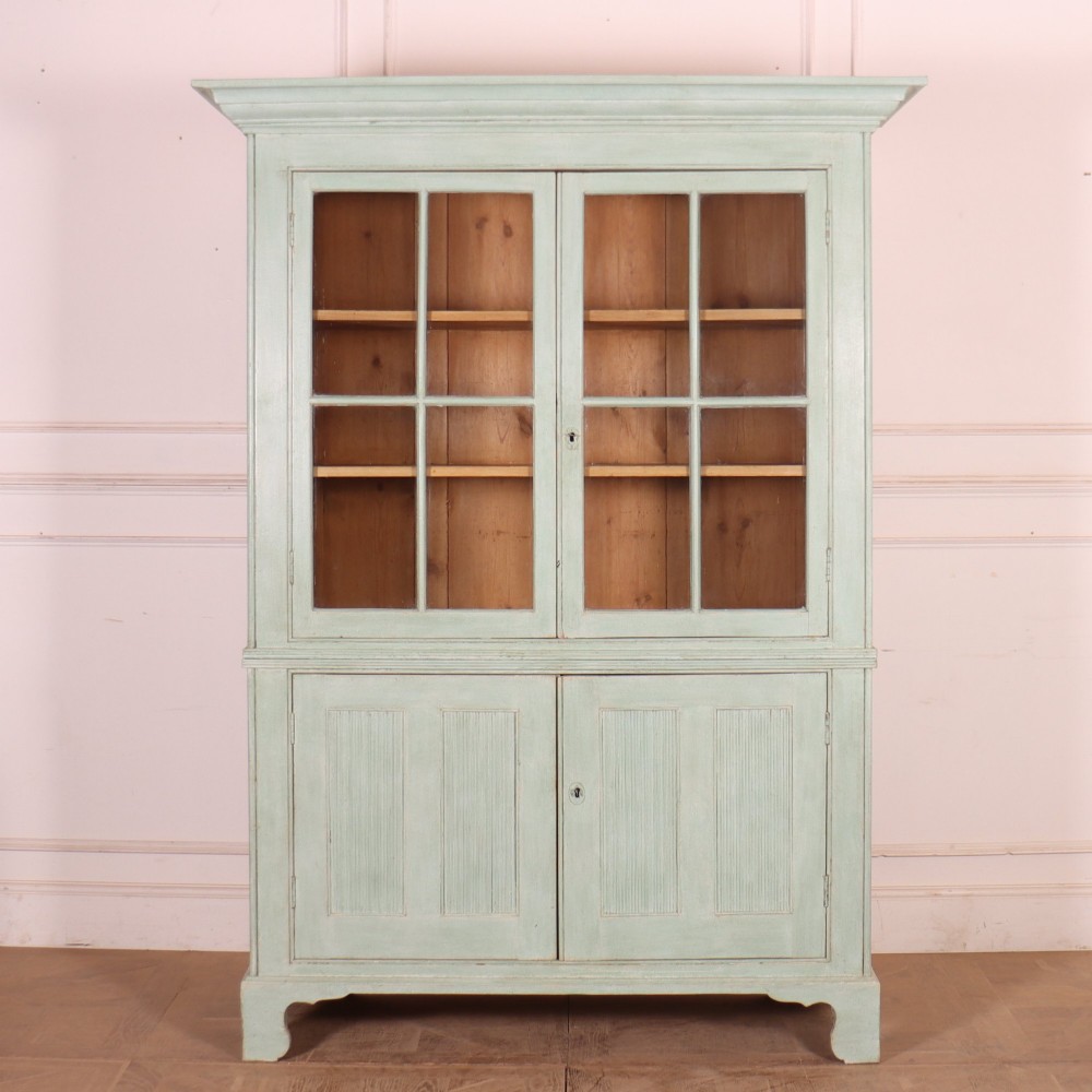 An English country painted pine dresser featuring two glazed upper doors revealing natural wood shelves above two panelled lower doors in a pale green finish.