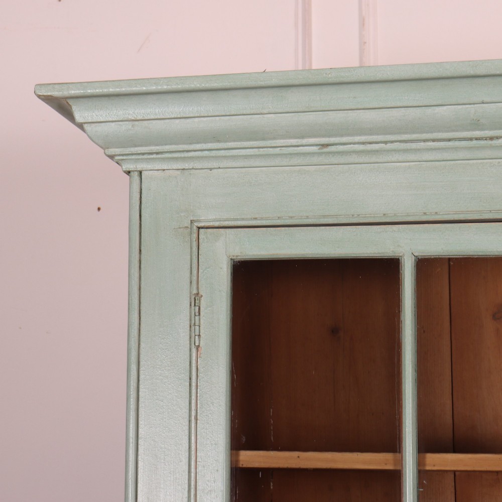 An English country painted pine dresser featuring two glazed upper doors revealing natural wood shelves above two panelled lower doors in a pale green finish. View II