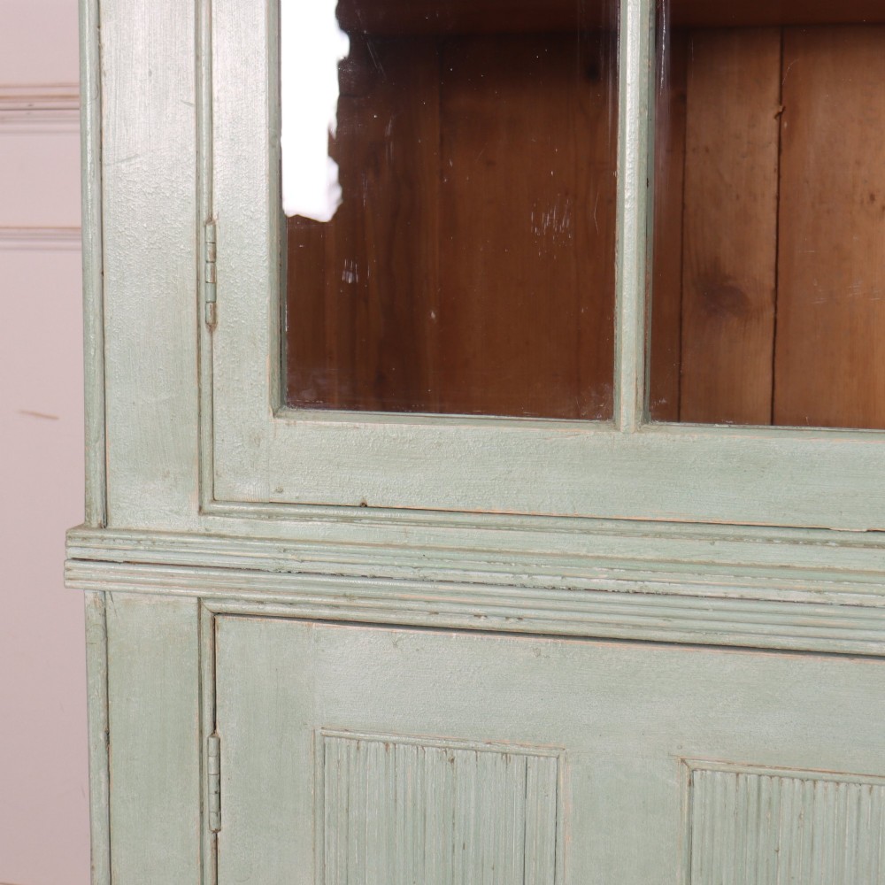 An English country painted pine dresser featuring two glazed upper doors revealing natural wood shelves above two panelled lower doors in a pale green finish. View V