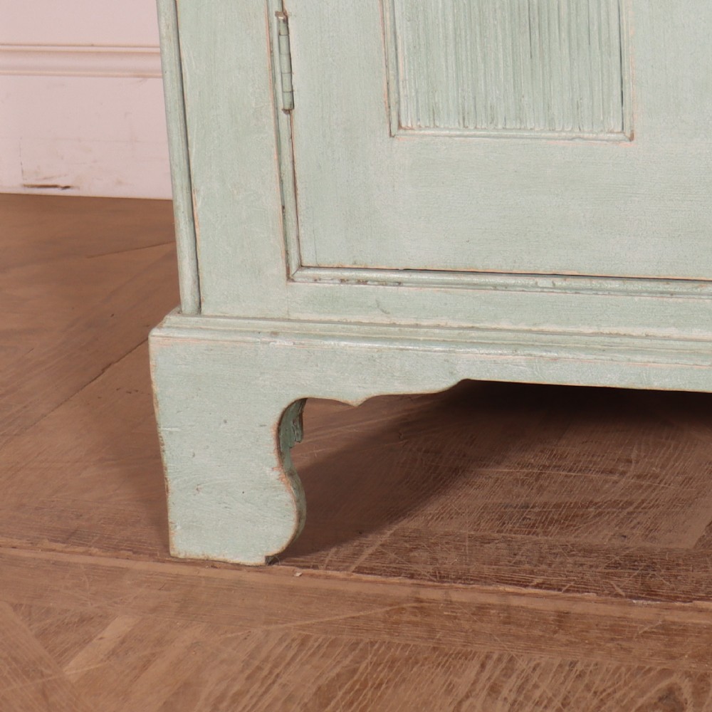 An English country painted pine dresser featuring two glazed upper doors revealing natural wood shelves above two panelled lower doors in a pale green finish. View VI