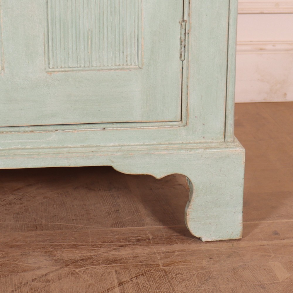 An English country painted pine dresser featuring two glazed upper doors revealing natural wood shelves above two panelled lower doors in a pale green finish. View VII