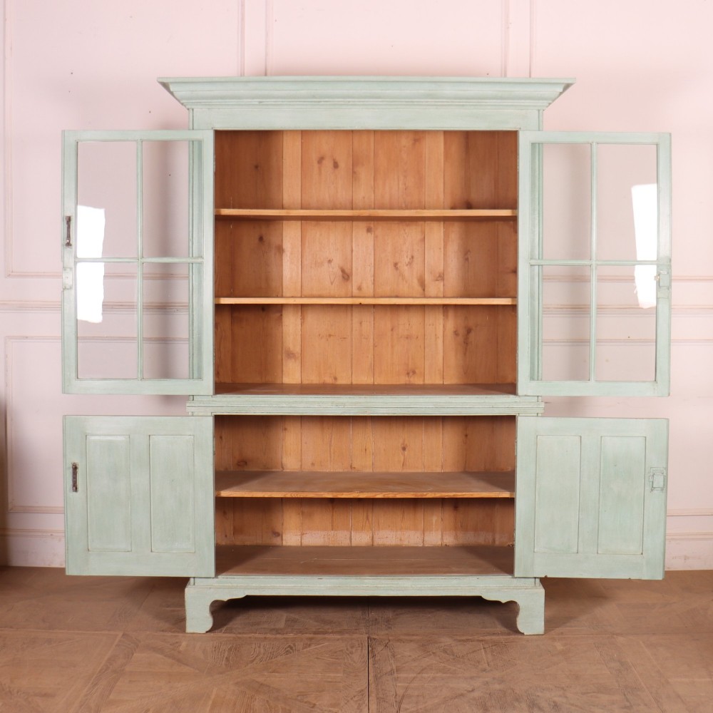 An English country painted pine dresser featuring two glazed upper doors revealing natural wood shelves above two panelled lower doors in a pale green finish. View VIII