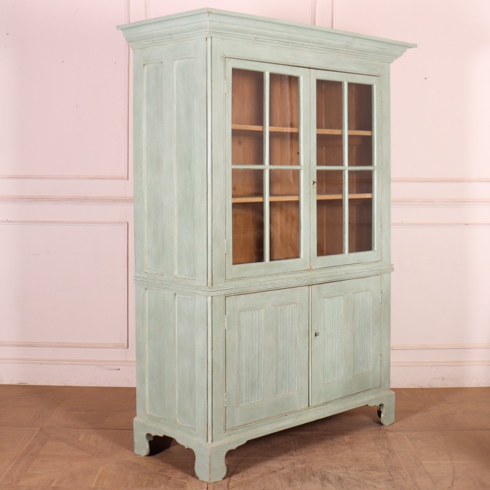 An English country painted pine dresser featuring two glazed upper doors revealing natural wood shelves above two panelled lower doors in a pale green finish. View IX