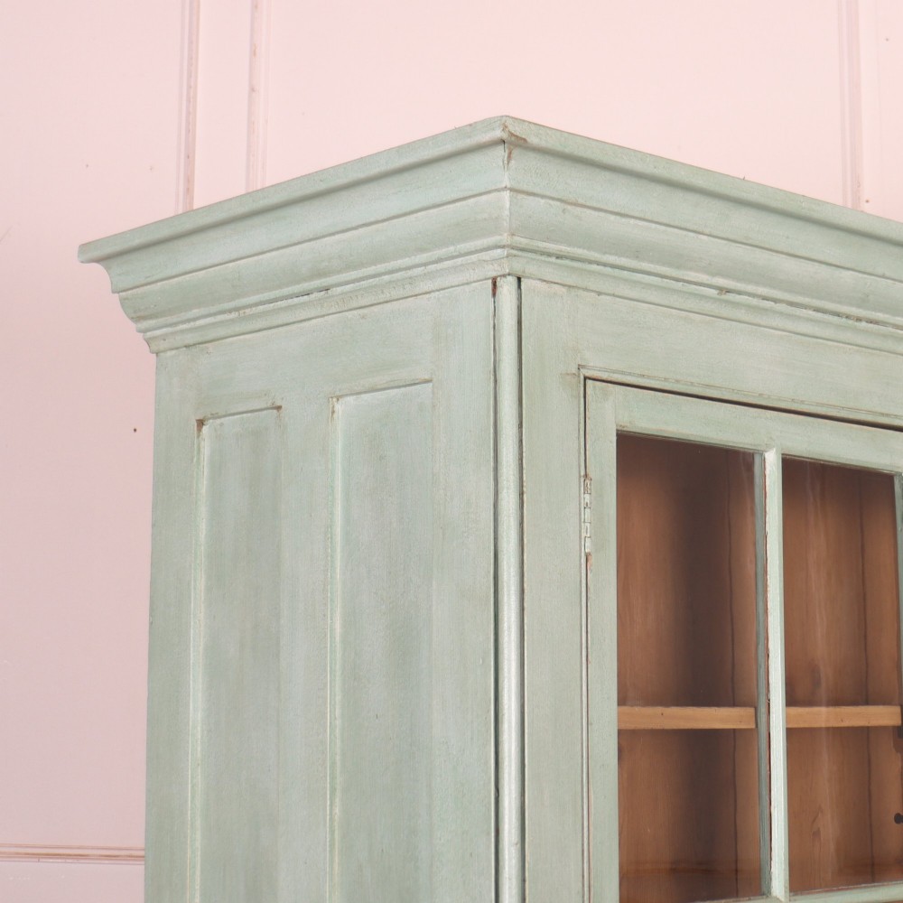 An English country painted pine dresser featuring two glazed upper doors revealing natural wood shelves above two panelled lower doors in a pale green finish. View X
