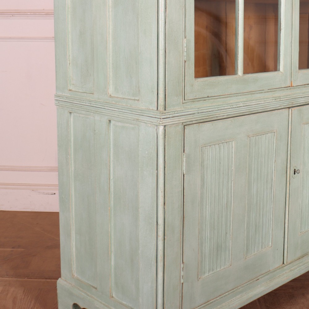 An English country painted pine dresser featuring two glazed upper doors revealing natural wood shelves above two panelled lower doors in a pale green finish. View XI