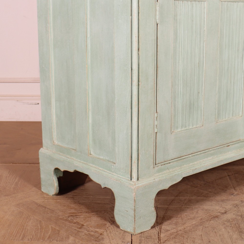 An English country painted pine dresser featuring two glazed upper doors revealing natural wood shelves above two panelled lower doors in a pale green finish. View XII