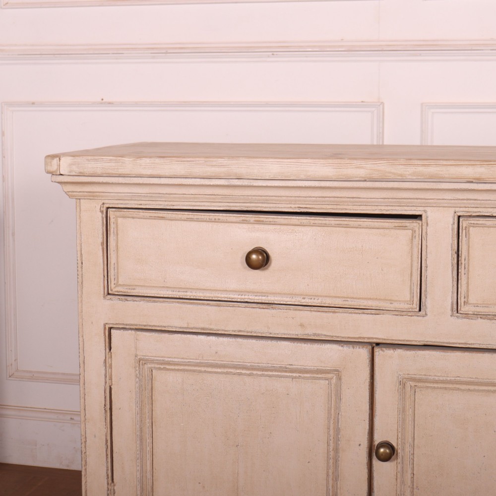 A large off-white painted English dresser base featuring four drawers above four cupboard doors with small brass knob handles. View II